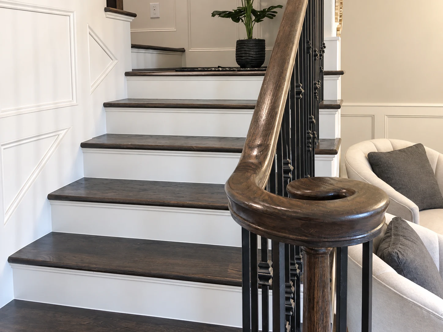 Wide view of dark stair treads, curved wood handrail, black metal balusters, and white paneled wall