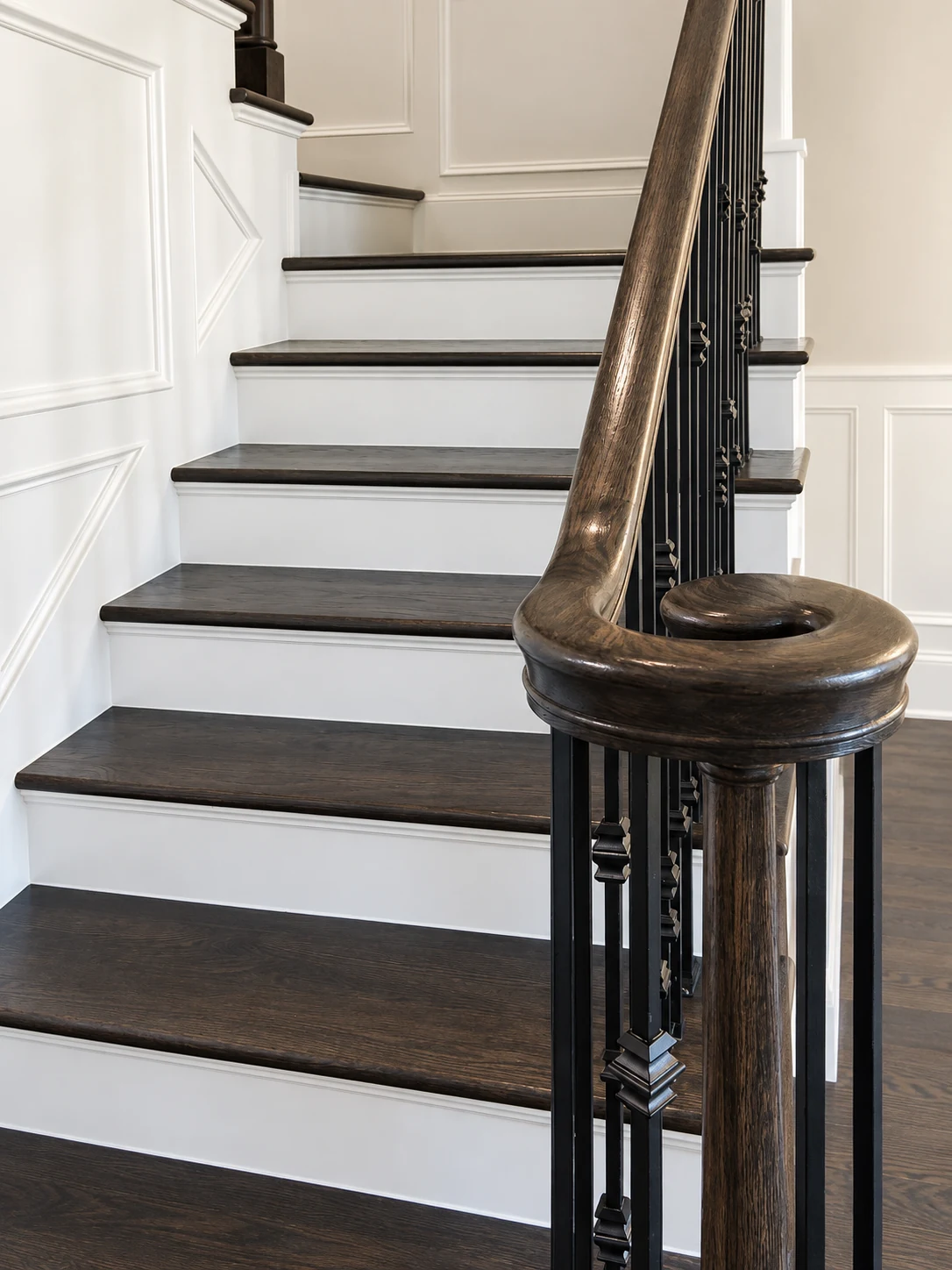 Close view of a staircase with dark wood treads and handrail, black balusters, and white paneled walls